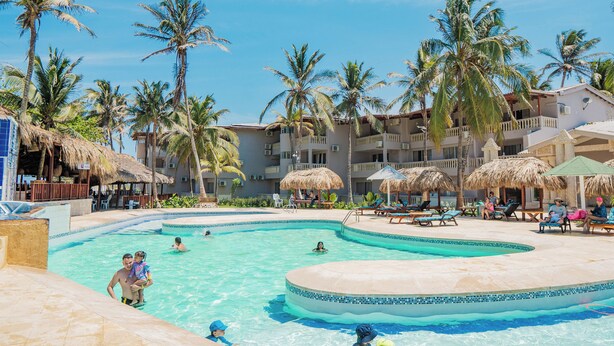 A resort pool area with palm trees, lounge chairs, and a building with balconies.