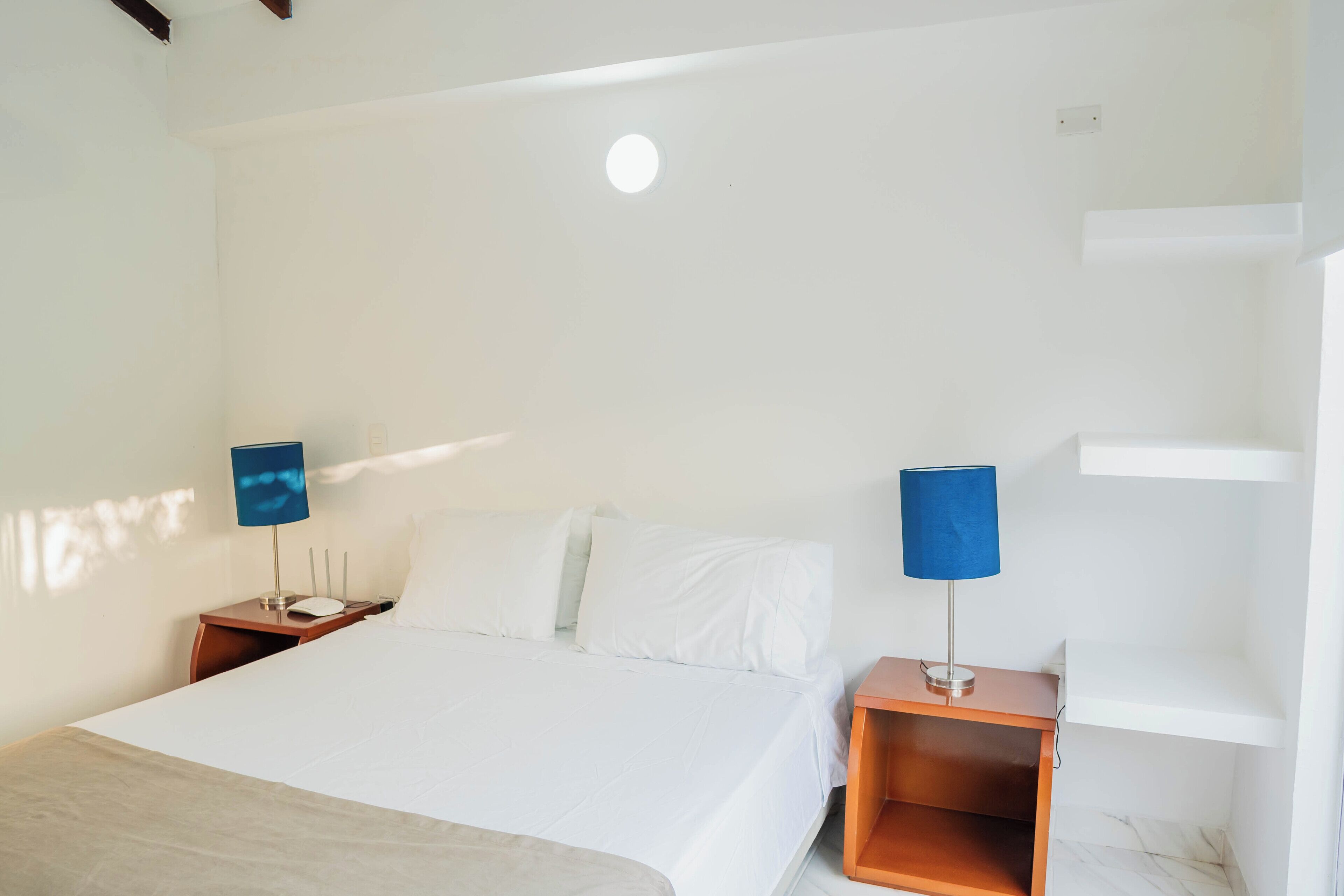 A hotel room with a large bed, two bedside tables with lamps, a white wall, and a ceiling light.