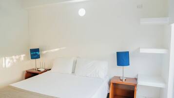 A hotel room with a large bed, two bedside tables with lamps, a white wall, and a ceiling light.