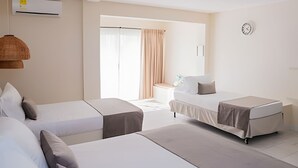 A hotel room with two single beds, a small table with a chair, a hanging lamp, and a large window with curtains.