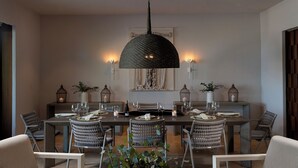 A dining area with a long table, wicker chairs, and a central hanging light fixture.