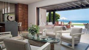 A modern living room with a glass coffee table, striped armchairs, and a view of the ocean.