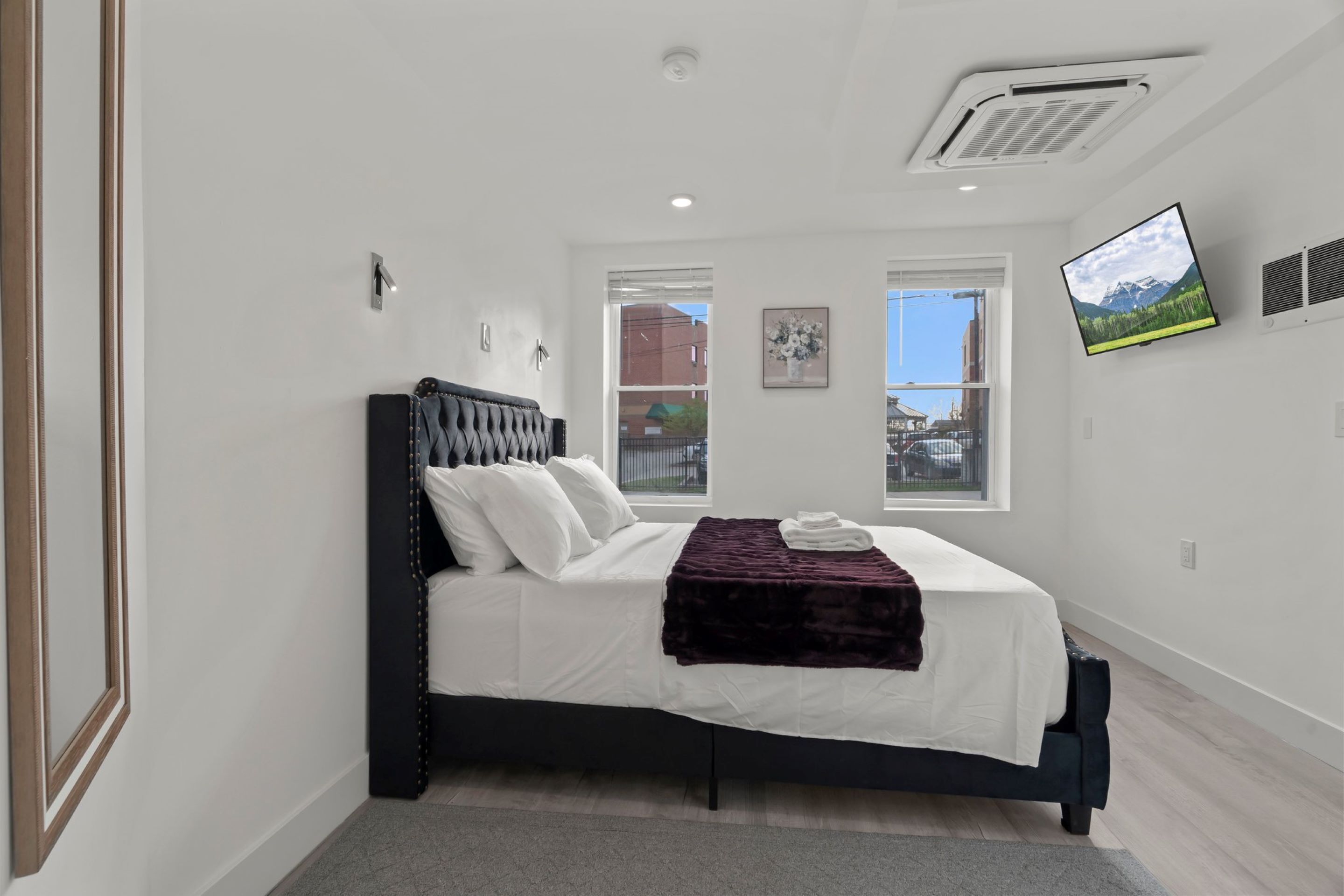 A modern bedroom with a bed, a flat-screen TV, and two windows.