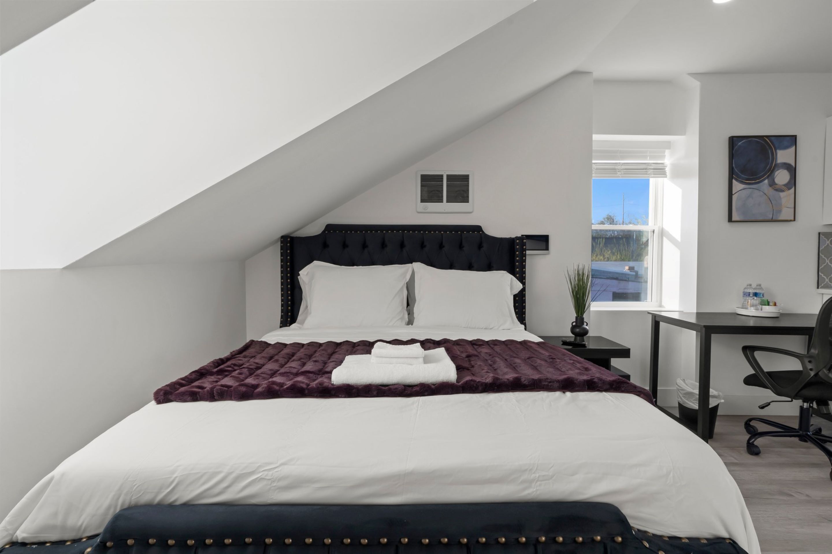 A modern bedroom with a large bed, a desk, and a chair.