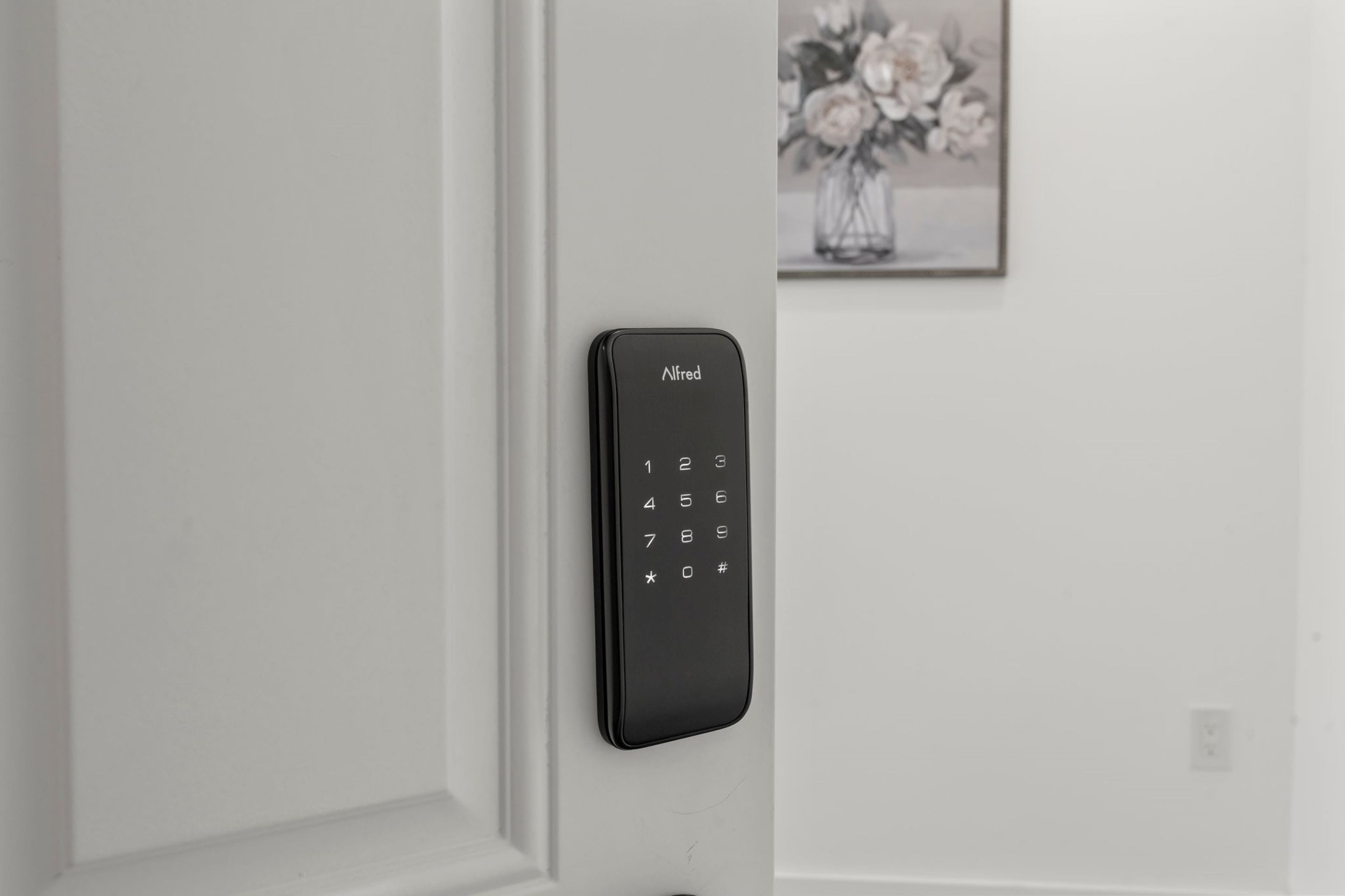 A black doorbell with the brand name 'Alfred' mounted on a white door.