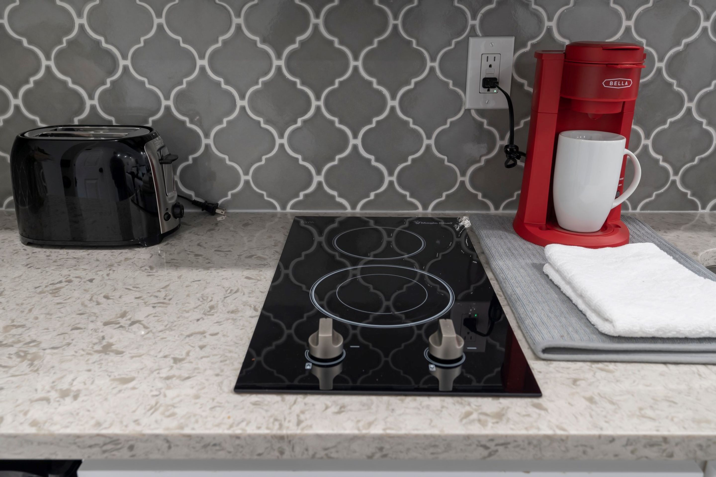 A kitchen with a black toaster, a red coffee maker, and a white mug on a countertop.