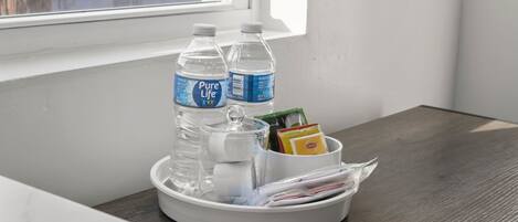 Een dienblad met twee flessen Pure Life water, een glas, een pak zakdoekjes en enkele tijdschriften op een houten tafel nabij een raam.
