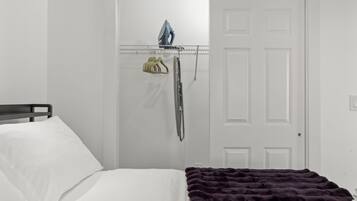 Un dormitorio con cama, una puerta y un tablero de planchar montado en la pared con plancha y perchero.