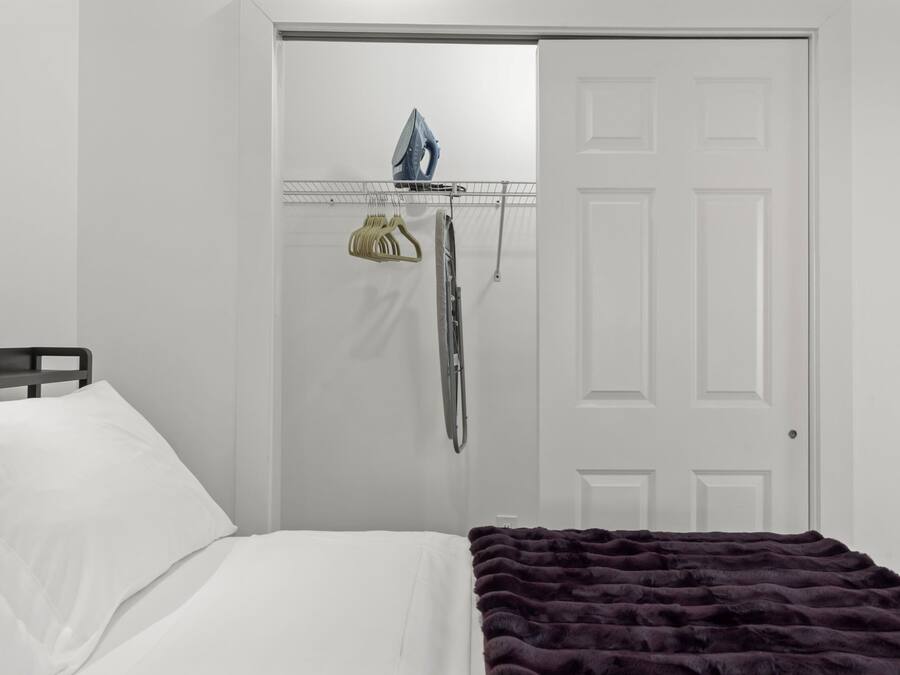 Un dormitorio con cama, una puerta y un tablero de planchar montado en la pared con plancha y perchero.