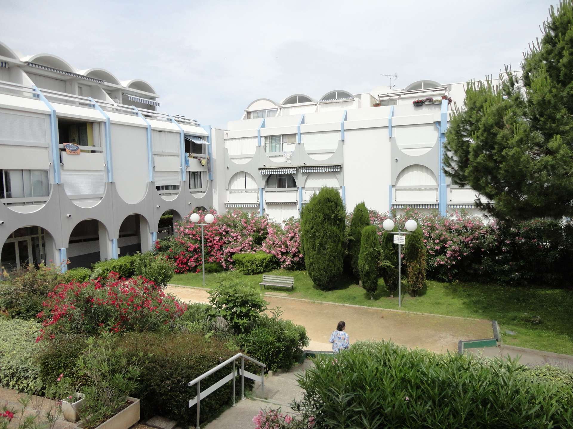A modern building with a courtyard featuring a central pathway, surrounded by lush greenery and flowering plants.
