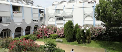 A modern building with a courtyard featuring a central pathway, surrounded by lush greenery and flowering plants.