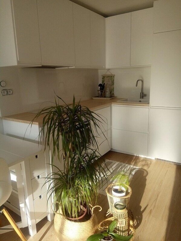 Een keuken met witte kastjes, een spoelbak, een potplant en een rieten bijzettafeltje met kaarsen.