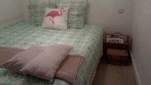 Un dormitorio pequeño y ordenado con cama, almohadas, una mesita de noche y un buró.
