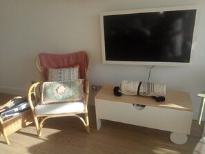 Une pièce comprenant une chaise en bois, une petite armoire blanche et un grand téléviseur noir fixé au mur.