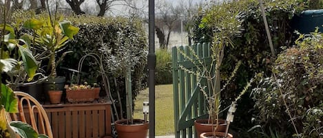 Un patio al aire libre con una mesa, sillas, un gran paraguas y plantas en macetas.