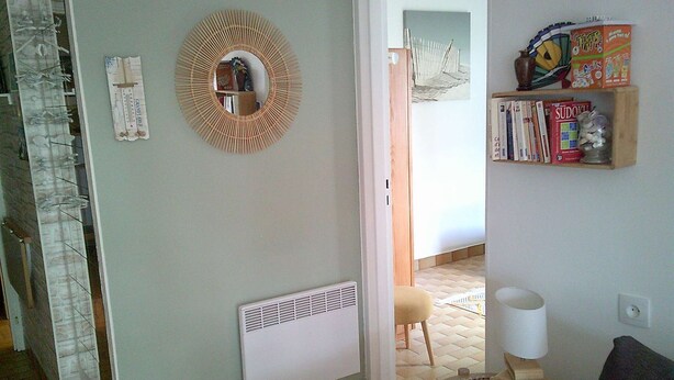 A room with a radiator, a round mirror, a bookshelf with books and a puzzle, and a chair.