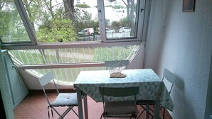 A small patio area with a table and chairs, a window with a view of the street, and a brick floor.