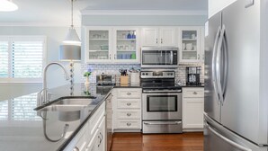 A modern kitchen with stainless steel appliances, white cabinetry, and a wooden floor. - Ocean Pearl! Amazing Ocean & Pier Views, Oceanfront Pool, In the heart of the Pier Village! (Saint Simons Island)