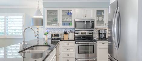 A modern kitchen with stainless steel appliances, white cabinetry, and a wooden floor.