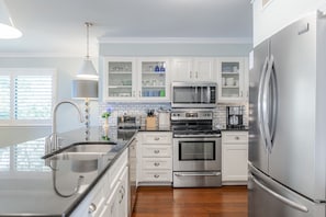 A modern kitchen with stainless steel appliances, white cabinetry, and a wooden floor. - Ocean Pearl! Amazing Ocean & Pier Views, Oceanfront Pool, In the heart of the Pier Village! (Saint Simons Island)