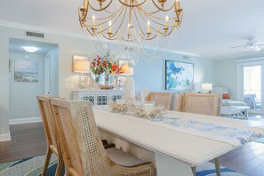 A dining area with a chandelier, wooden chairs, a white table, and a floral centerpiece. - Ocean Pearl! Amazing Ocean & Pier Views, Oceanfront Pool, In the heart of the Pier Village! (Saint Simons Island)