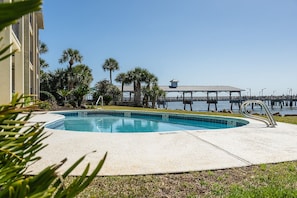 A swimming pool with a deck, surrounded by palm trees and a pier extending into the water. - Ocean Pearl! Amazing Ocean & Pier Views, Oceanfront Pool, In the heart of the Pier Village! (Saint Simons Island)
