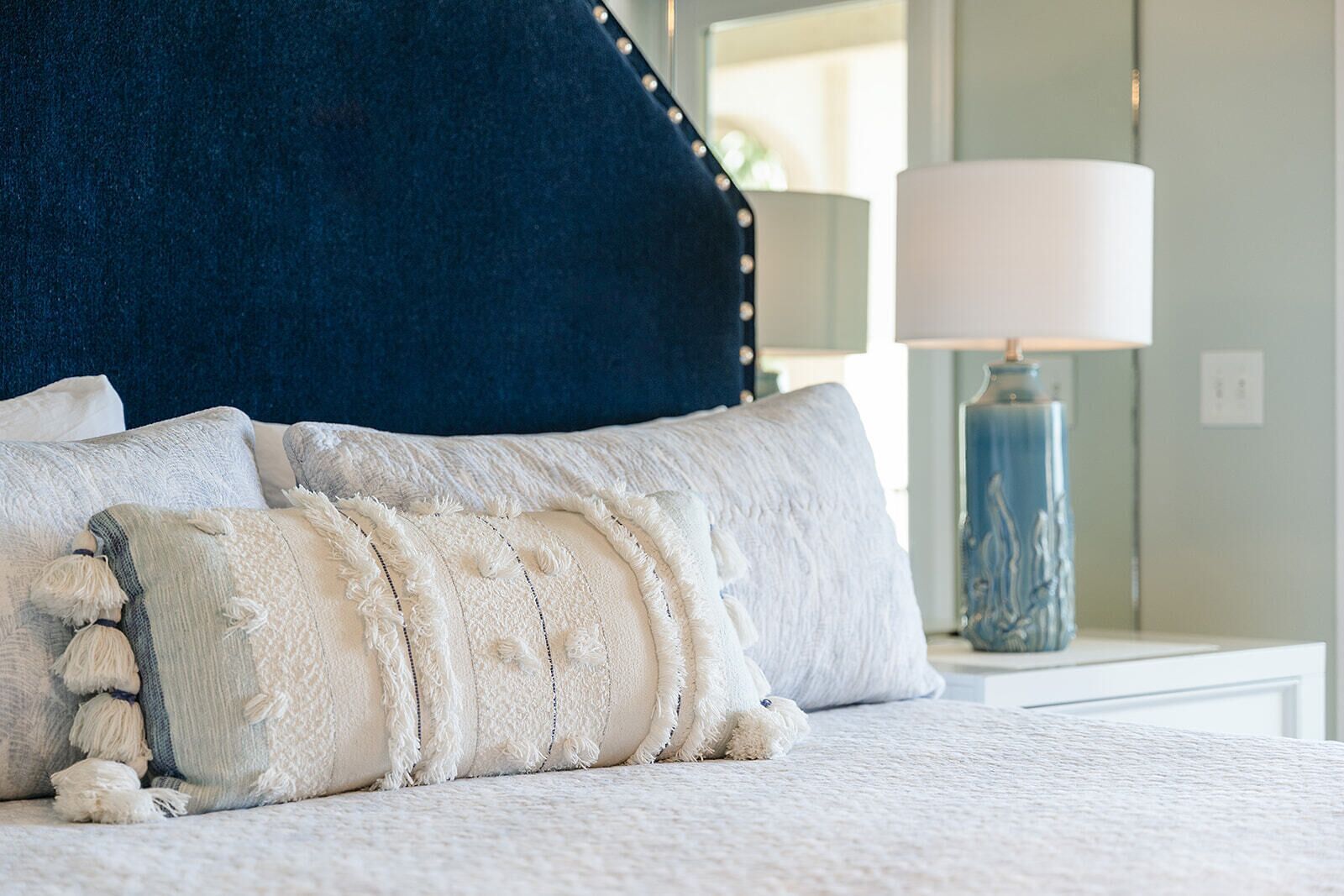 Un lit avec une literie blanche, une tête de lit bleu foncé et une lampe décorative sur une table de chevet.