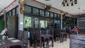 A restaurant interior with wooden tables and chairs, a deer head decoration, and large windows. - Buengngarm Resort (Bung Khong Long)