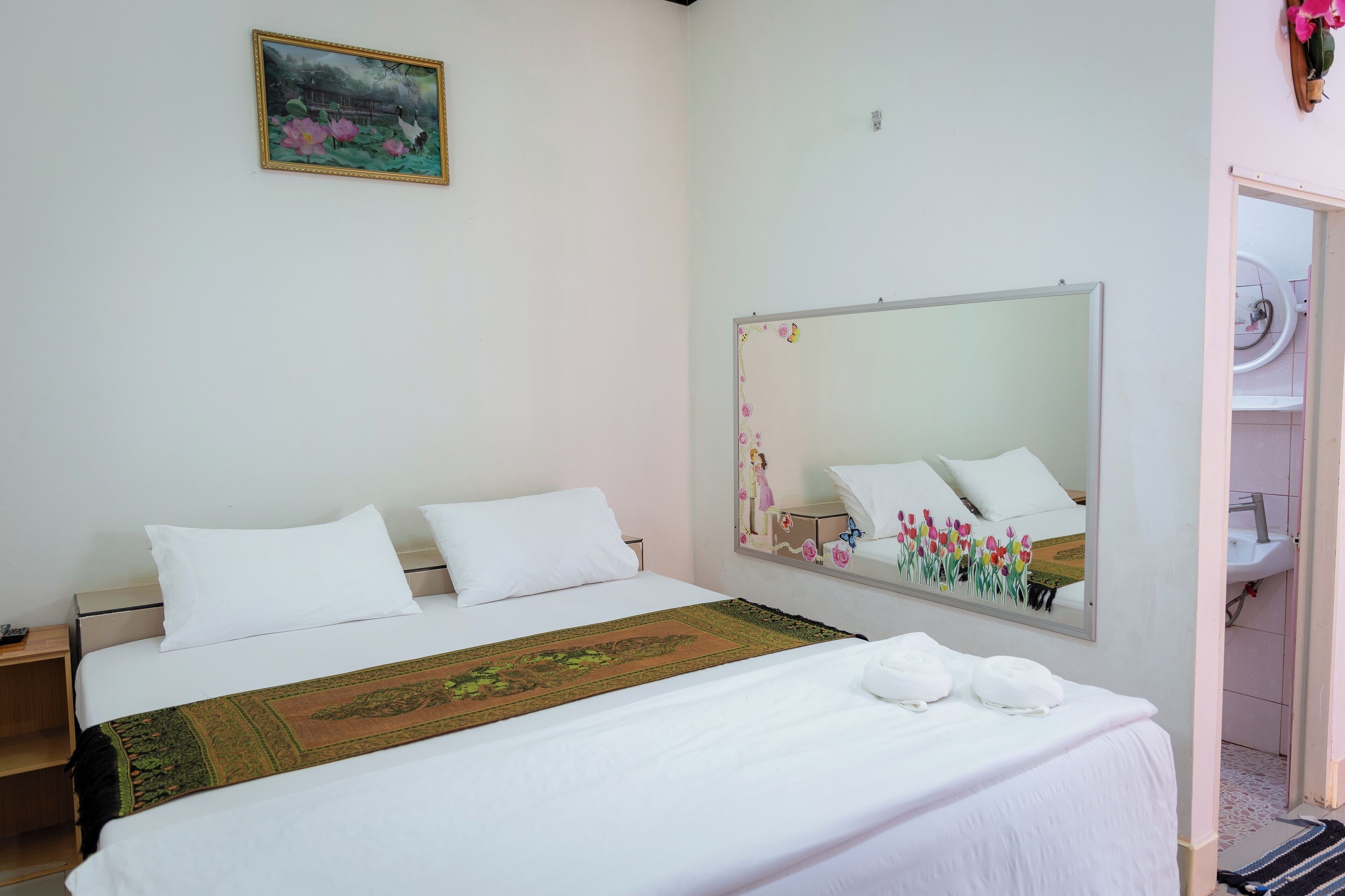 Habitación de hotel con cama, mesita de noche, espejo y baño visible a través de una puerta abierta.