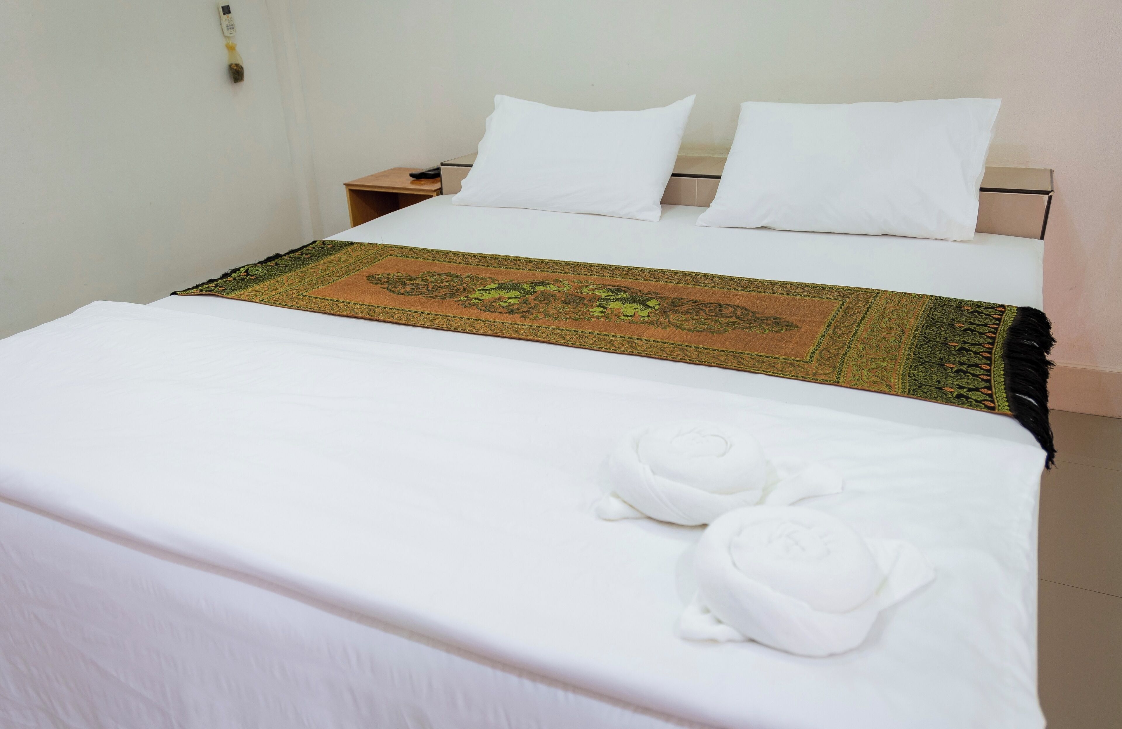 A neatly made bed with white linens, a decorative bedspread, and two rolled towels.