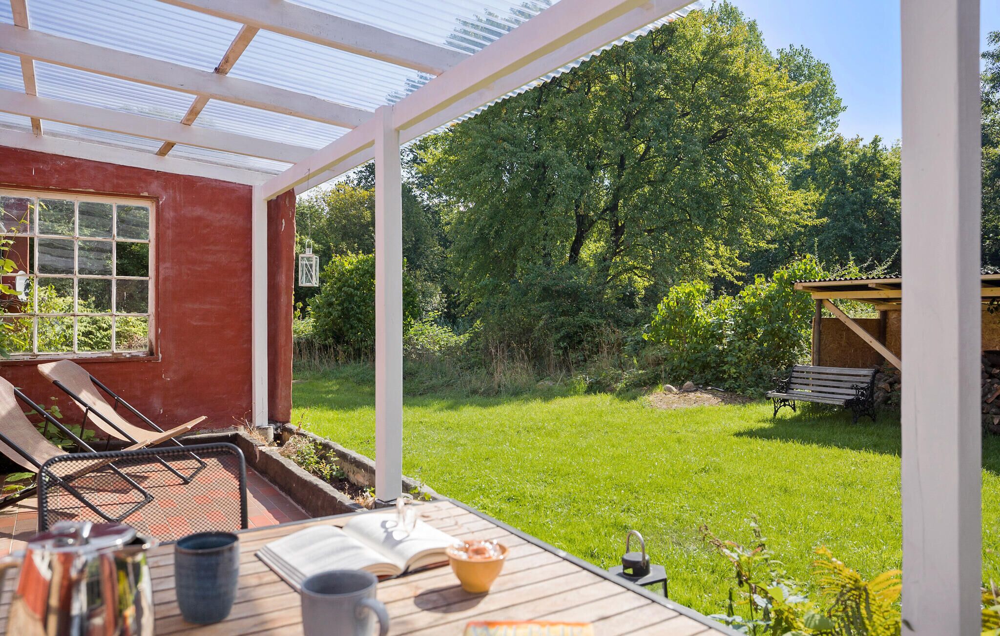 Eine überdachte Terrasse mit Tisch, Stühlen und einer Bank.