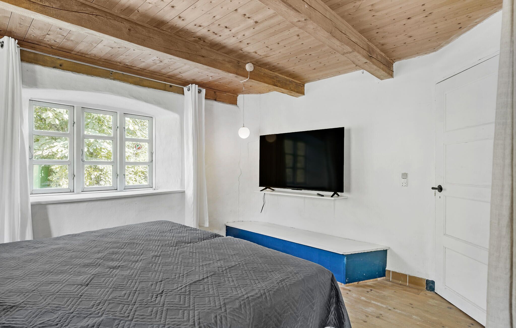 A bedroom with a bed, a TV mounted on the wall, a window, and a door.