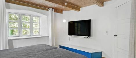 A bedroom with a bed, a TV mounted on the wall, a window, and a door.