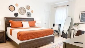 Ein Schlafzimmer mit einem hölzernen Bett, orangefarbener Bettwäsche, einem Nachttisch, einem Sessel und einem Spiegel.
