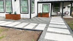 Ein modernes, zweistöckiges Haus mit großen Fenstern, einer Veranda und einem Kiesweg, der zum Eingang führt.