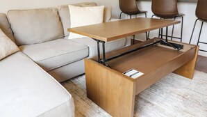 A modern living room with a sofa, a wooden coffee table with a hidden drawer, and a kitchen area in the background.