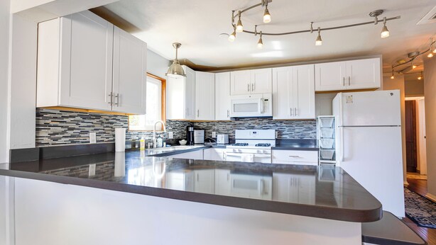A modern kitchen with white cabinets, a large island, a microwave, and a refrigerator.