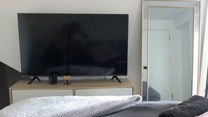 Makuuhuone, jossa on sänky, seinälle kiinnitetty taulutelevisio ja puinen yöpöytä sekä peili seinässä.