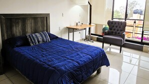 Un dormitorio con una cama grande, una silla, una mesita y un ventanal con vistas al exterior.