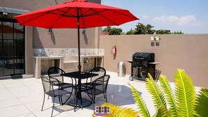 Un patio al aire libre con una mesa, sillas, un paraguas rojo, una parrilla y un revoque de cerámica.