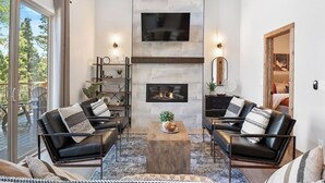 A modern living room with a fireplace, two leather sofas with patterned cushions, a coffee table, and a large window overlooking a deck. - Alpine View: Your Getaway to Mountain Adventures (Angel Fire)