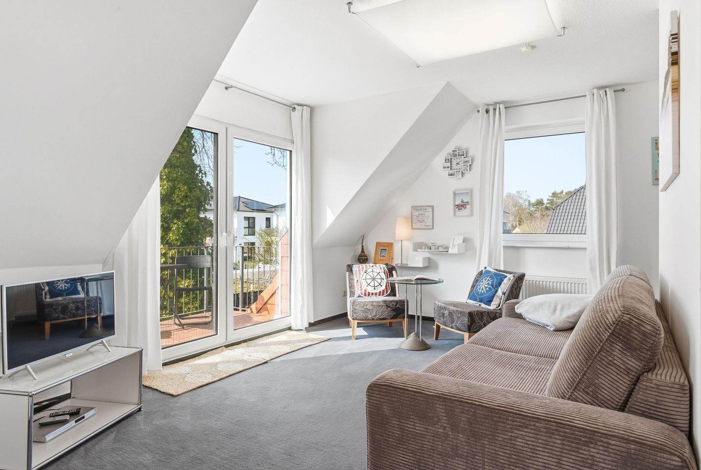 A modern living room with a TV, sofa, and a balcony with a view of the outside.