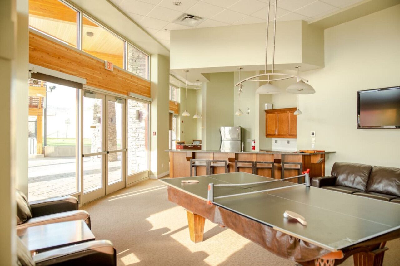 Une pièce spacieuse équipée d’une table de ping-pong, d’un canapé et d’un coin cuisine avec des meubles en bois et un réfrigérateur.