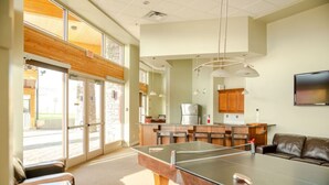A spacious room with a ping pong table, a sofa, and a kitchen area with wooden cabinets and a refrigerator.