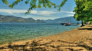 A lakeside view with boats docked, a clear sky, and mountains in the background.