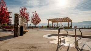 A park with a stone building, a wooden pergola, and a bench.