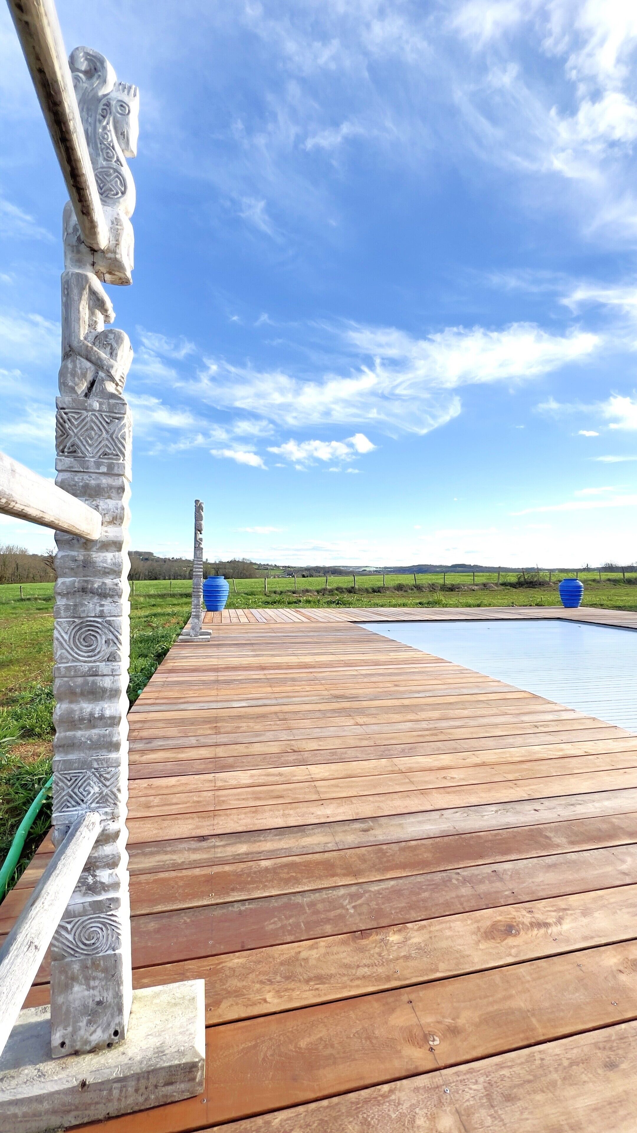 Une terrasse en bois qui mène à une piscine, avec un ciel dégagé.