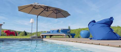 Un espace aménagé au bord de la piscine, comprenant un fauteuil de relaxation, un grand parasol et une statue de taureau décorative.