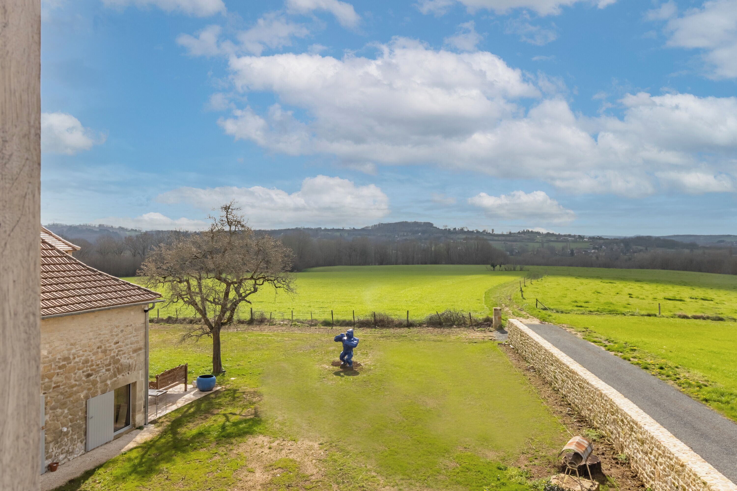 A rural landscape with a stone building, a grassy field, and a road.