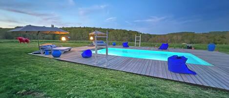 A swimming pool with a wooden deck, lounge chairs, and a covered seating area.